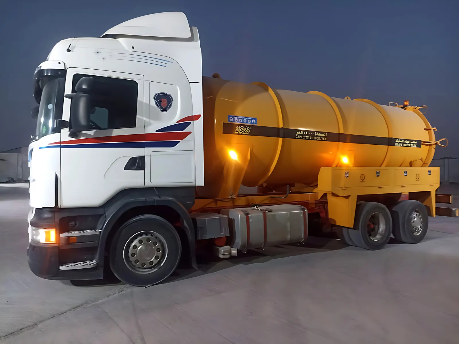 A Desert Rock wastewater vacuum truck with its lights on at dusk
